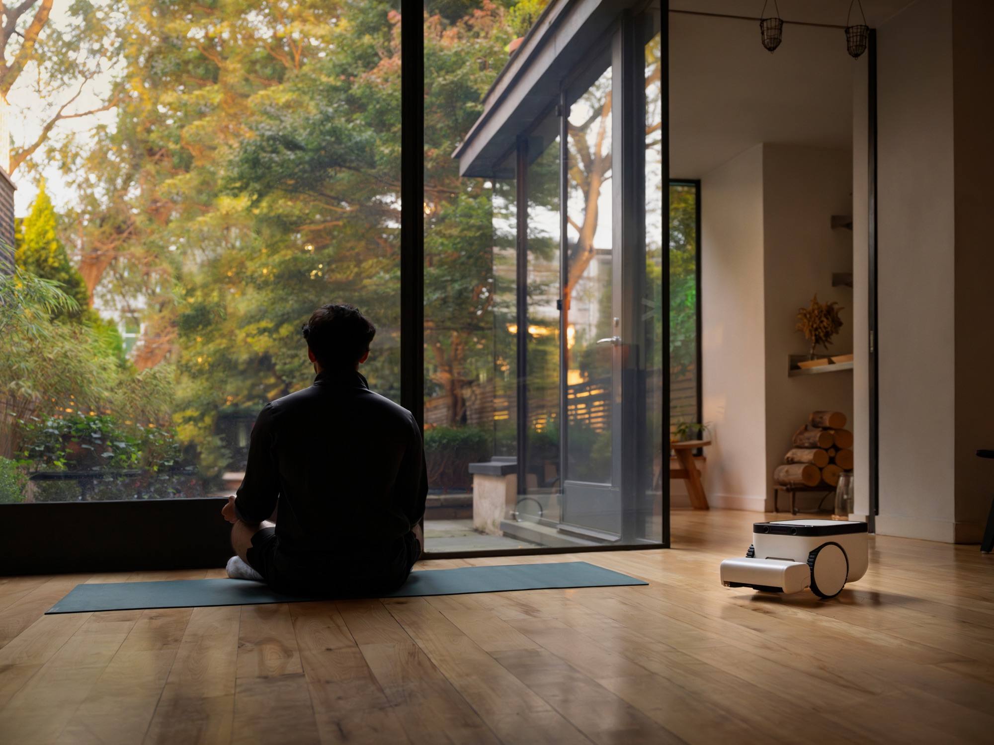 Matic cleaning a hardwood floor while a person sits on a yoga mat