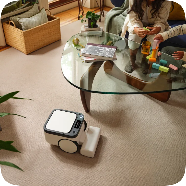 Matic robot cleaning carpet under a glass coffee table while a family plays