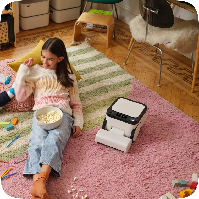 Matic robot vacuum cleaning popcorn off a striped rug next to a child